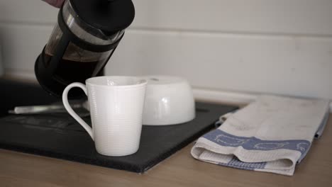 Pouring-hot-coffee-from-a-french-press-into-a-white-ceramic-coffeecup,-filmed-in-slow-motion