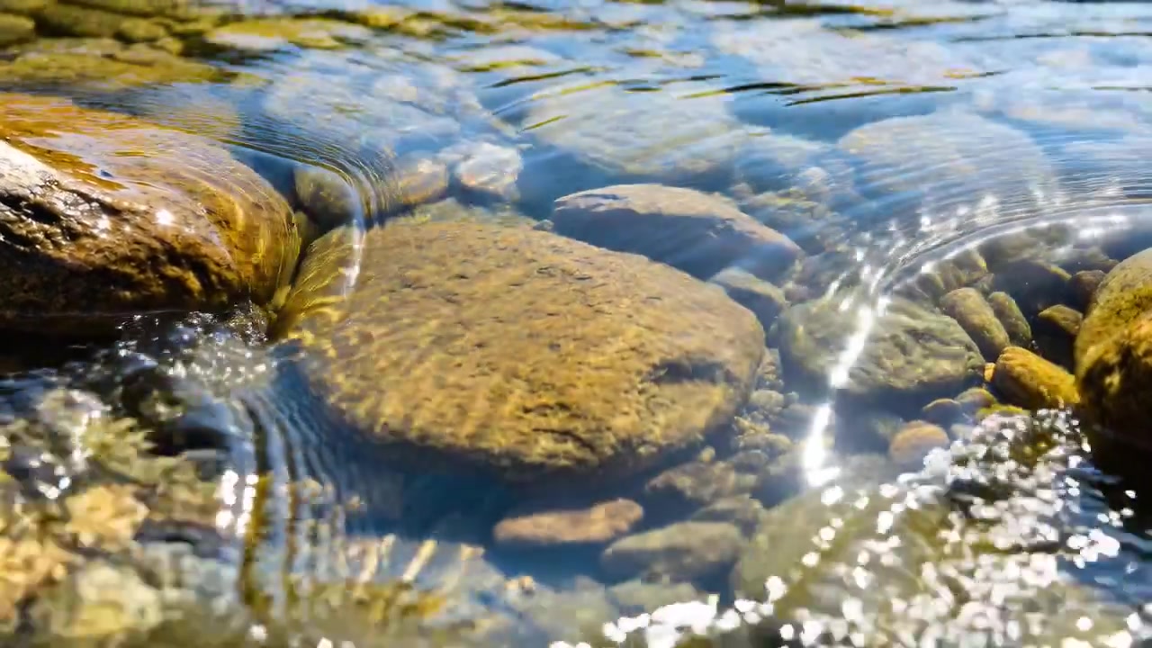 L'acqua che scorre crea increspature dopo che un sasso schizza su una pietra piatta in un ruscello illuminato dal sole, con caustiche.