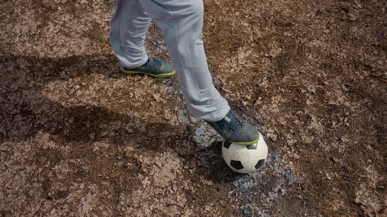 Balón atrapado en solitario sobre terreno marcado, contacto preciso y equilibrio en ritmo lento; interacción aérea cercana con el pie, texturas de campo embarrado y ambiente de entrenamiento centrado para tutoriales de entrenamiento y técnica