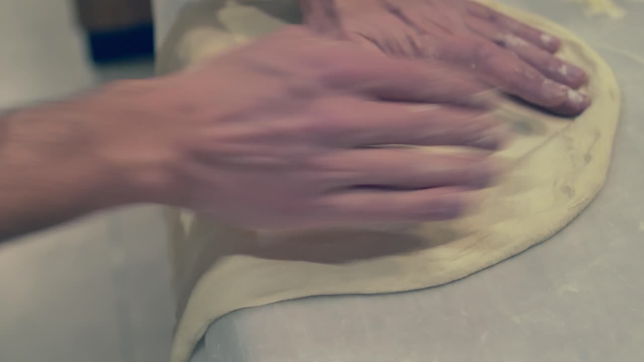 итальянский повар растягивает и переворачивает тесто для пиццы с помощью края стола и силы тяжести