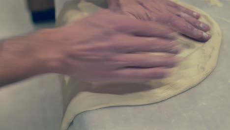 chef italiano estirando y girando la masa de pizza usando el borde de la mesa y la gravedad