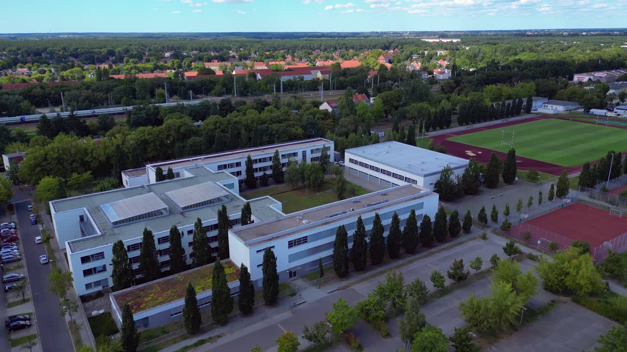 Hennigsdorf High School showcasing its modern architecture, sports facilities, parking area, surrounding urban landscape. Fabulous aerial view flight fly push forward drone