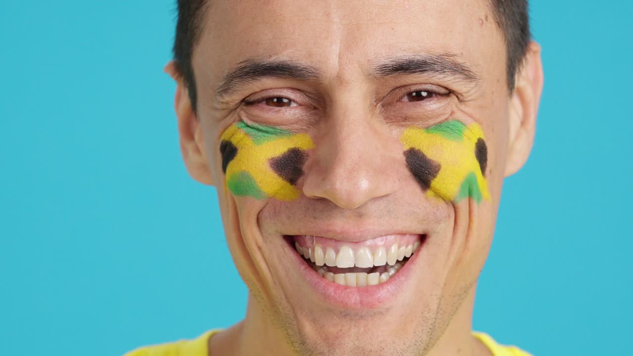 Man with a jamaican flag painted on the face smiling