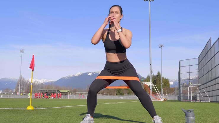 Veltrænet ung kvinde, der træner walking squats med træningselastik i slowmotion