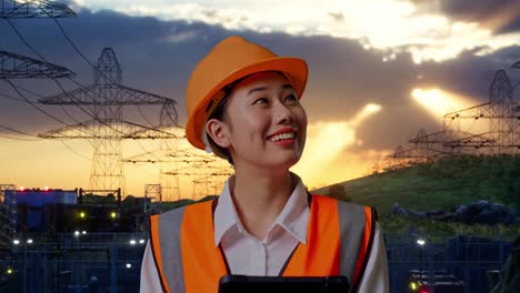 close up of asian female engineer with safety helmet looking at the tablet in her hand and looking around while standing near high voltage tower