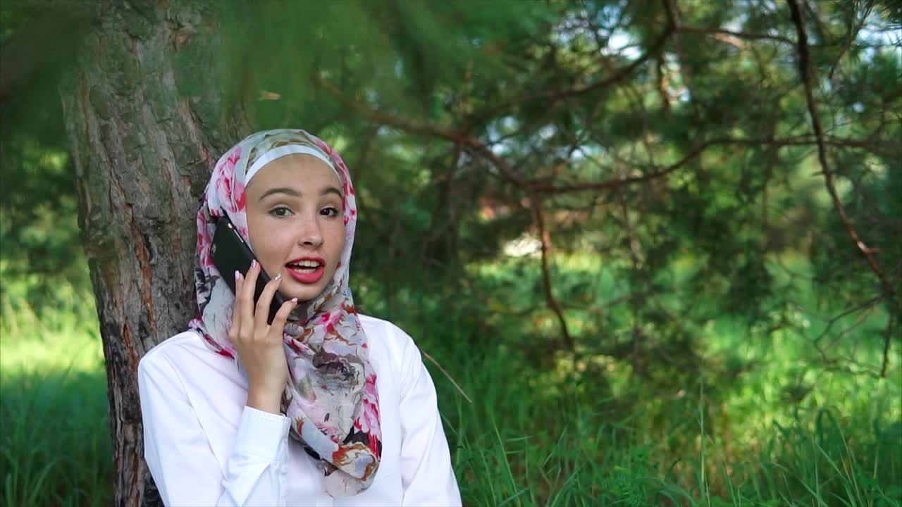 Young woman in hijab talking on phone in a park