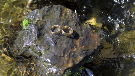 Two-wedding-rings,-side-by-side,-on-a-s-stone-surrounded-by-water