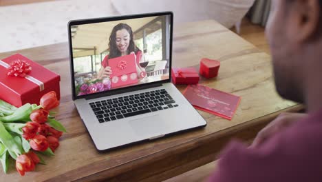 Happy-biracial-woman-with-vitiligo-opening-gift-and-making-valentine's-day-video-call-on-laptop