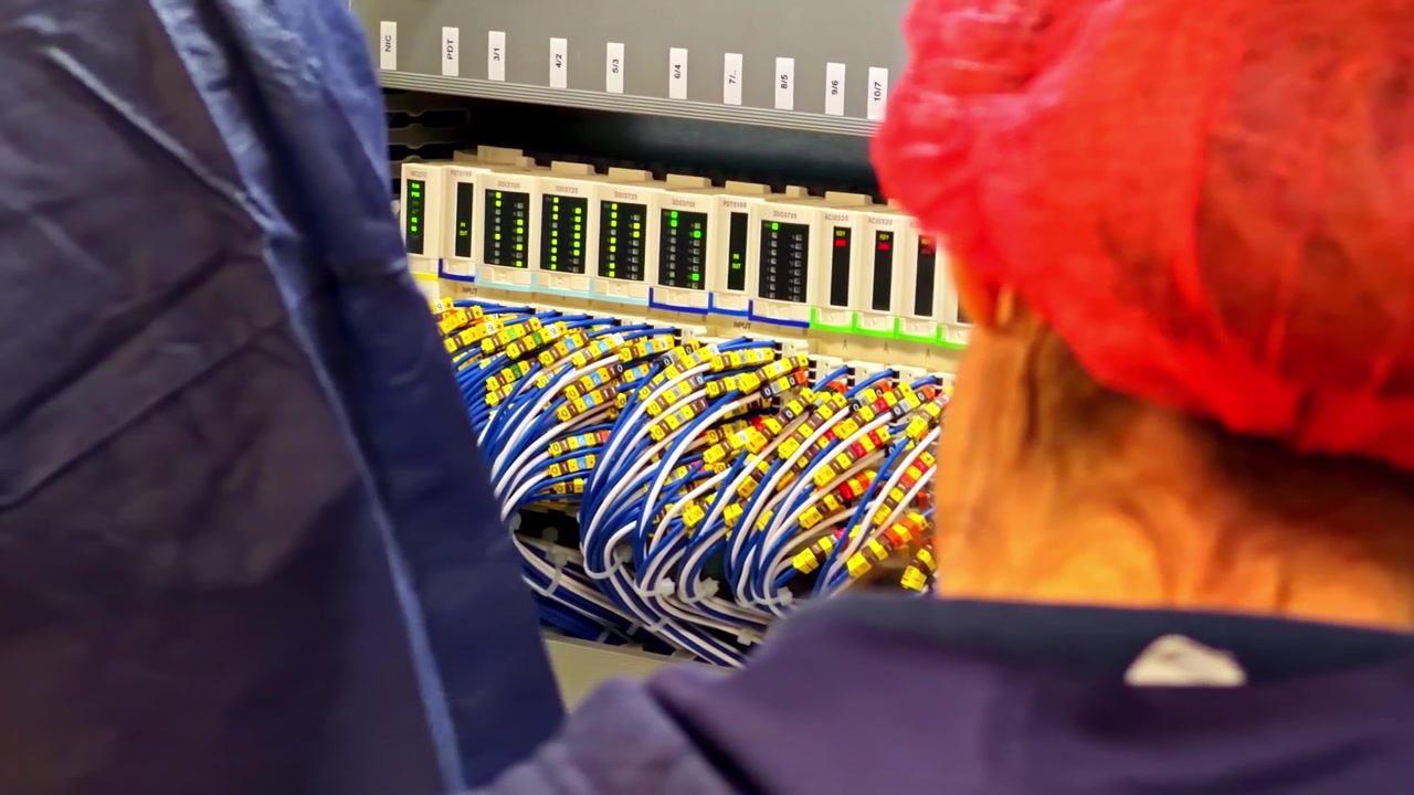 Technician in hair net inspects network cables connected to control panel in facility