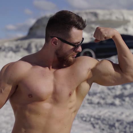 muscular sportsman outdoors. handsome shirtless man showing his arm biceps while standing on white canyon on black car background in summer day. close-up.