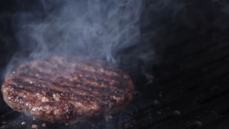 watch a burger patty cook on a grill, with smoke and a brief flame flare-up.