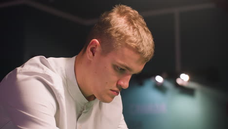 close up of young man in white shirt with intense focus, captured in dimly lit environment. camera highlights facial expression with soft lighting, deep concentration against dark background