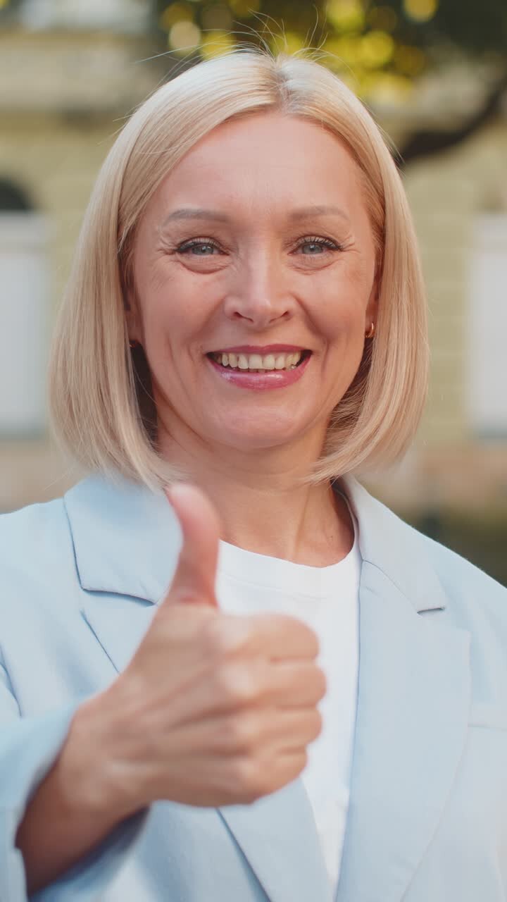 Sorridente donna d'affari bionda caucasica matura in abito formale che guarda la fotocamera e mostra il pollice in su