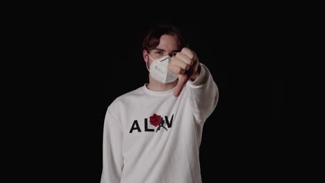 trendy young man giving thumbs down wearing mask, wide, black background