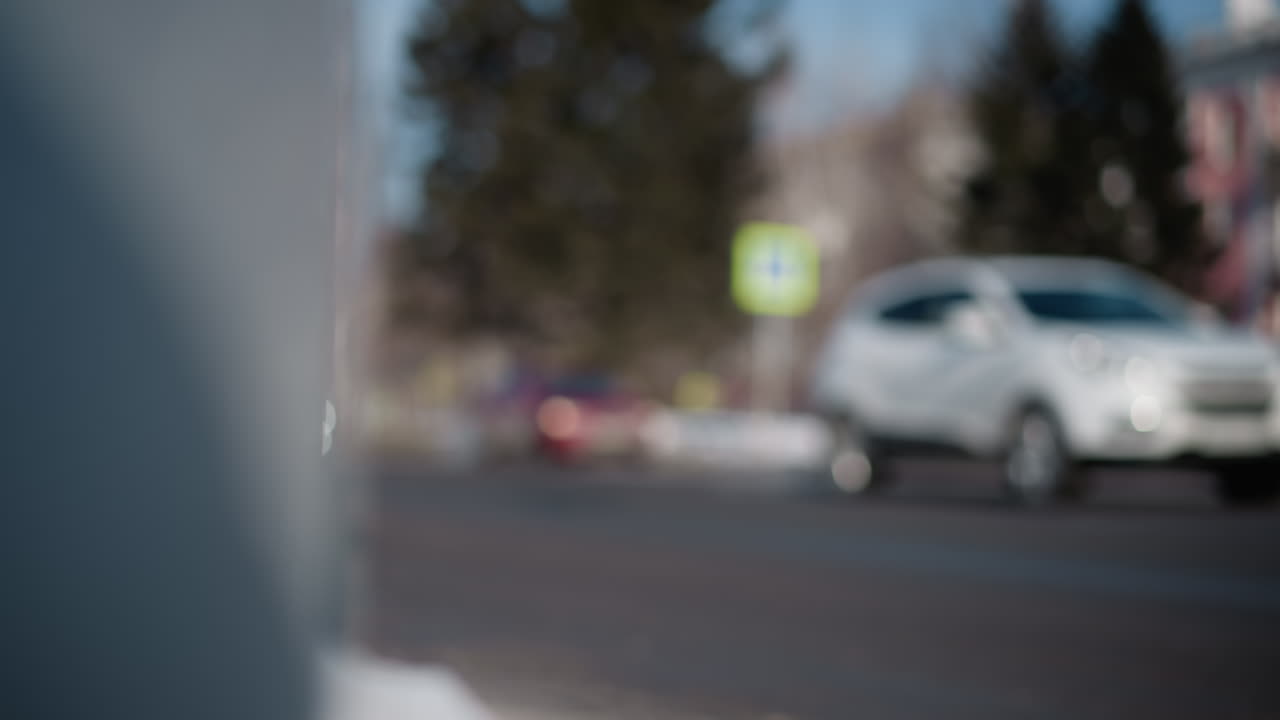 busy city street shows blur cars in soft focus, suv rolls by, buildings fade into bokeh, curb sets urban commute mood, winter light, tree and signs, captured from street perspective