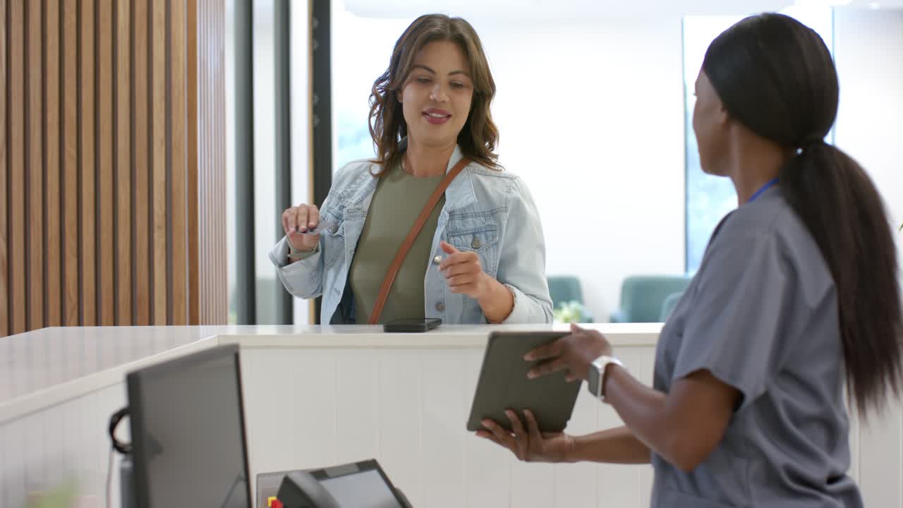Afroamerikansk kvinde, receptionist, bruger tablet og udveksler ID ved ankomst til klinik for check-in