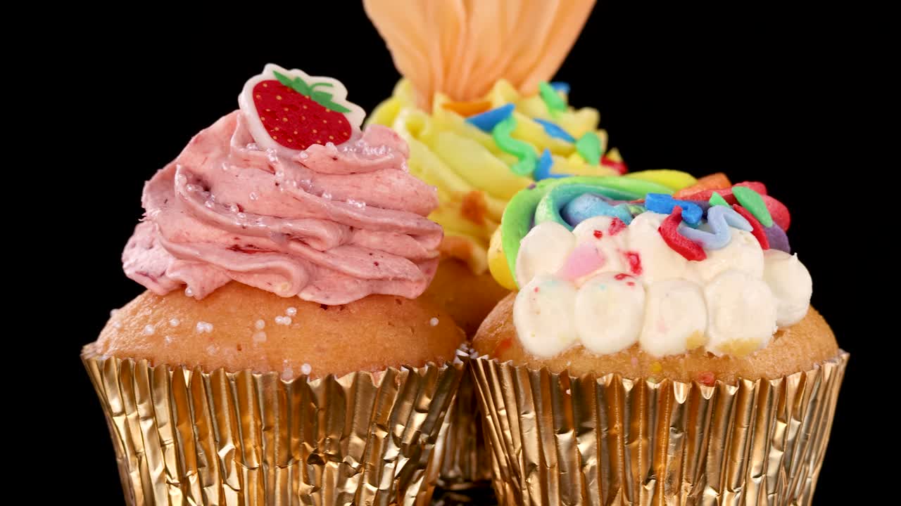 Colorful cupcakes with vibrant frosting and sprinkles rotate on black background under bright studio lighting