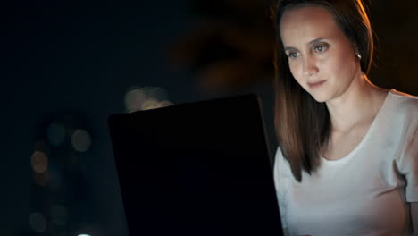 Eine-Junge-Frau-Sitzt-In-Einer-Sommernacht-Auf-Dem-Rasen-In-Der-Stadt,-Schaut-Auf-Den-Laptop-Bildschirm-Und-Schreibt-Eine-Nachricht-Auf-Die-Tastatur.-Freiberufliche-Programmiererin.-Nachtarbeit-Aus-Der-Ferne