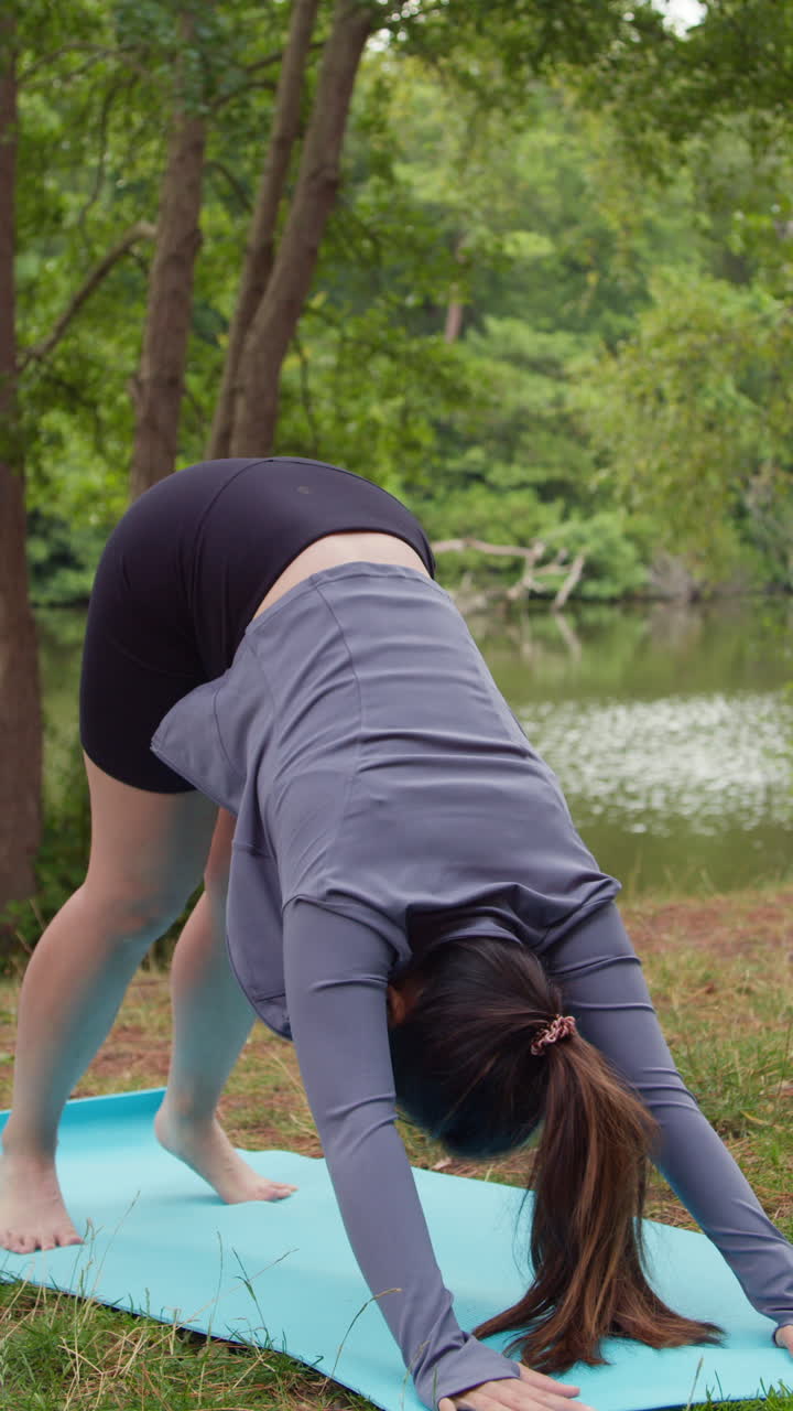 video vertical de una mujer con ropa deportiva haciendo yoga se estira en una alfombra en el bosque junto a un lago o río disfrutando de la paz y la belleza de la naturaleza filmado en tiempo real 2