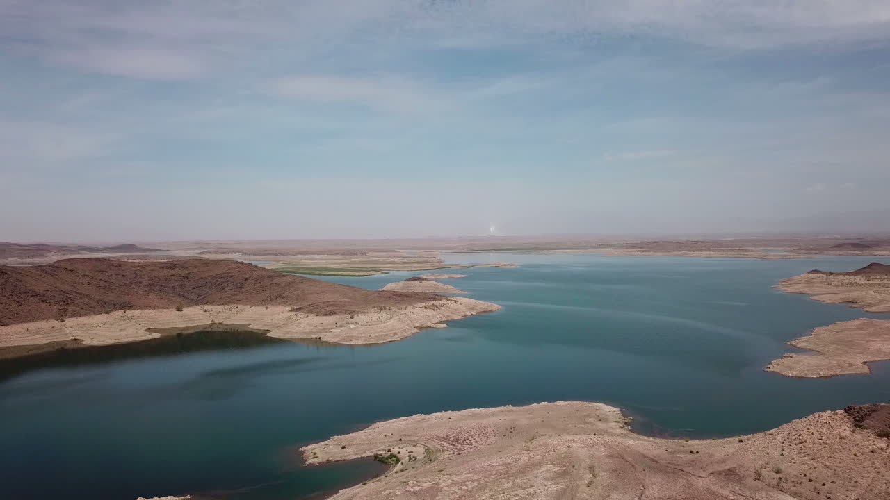 Panorama aereo grandangolare cinematografico 4K di un enorme bacino idrico in un paesaggio desertico aspro. Ripresa dall'alto con drone che mostra la scala dell'accumulo d'acqua e il contrasto ambientale nelle regioni aride.