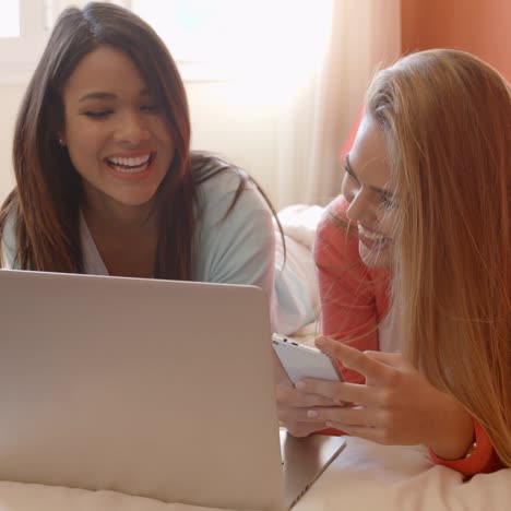 two happy friends with laptop lying on bed