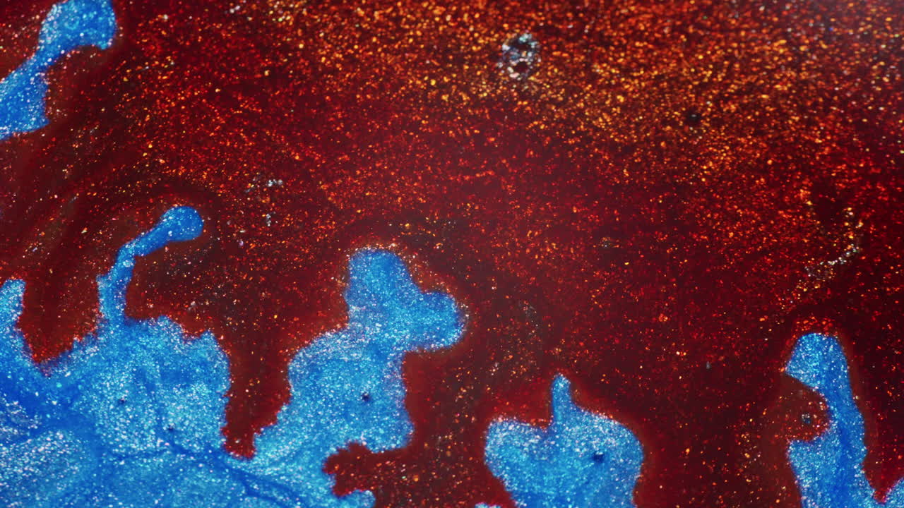 Macro view of iridescent blue ink reacting as red ink is added, creating fluid movement and dynamic displacement across the shimmering surface