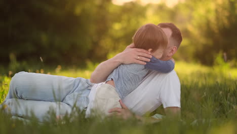 dad and son hugging lying in the meadow at sunset.