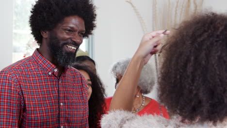 couple exchanging gifts as multi generation family celebrate christmas at home together
