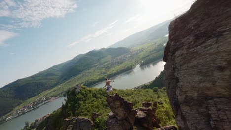 guy on top of mountain ridge, fast drone fpv, aerial shot with speed, king of the world pose, mountainclimber, person on top of hill, danube river valley landscape overview, flying around, flying fast