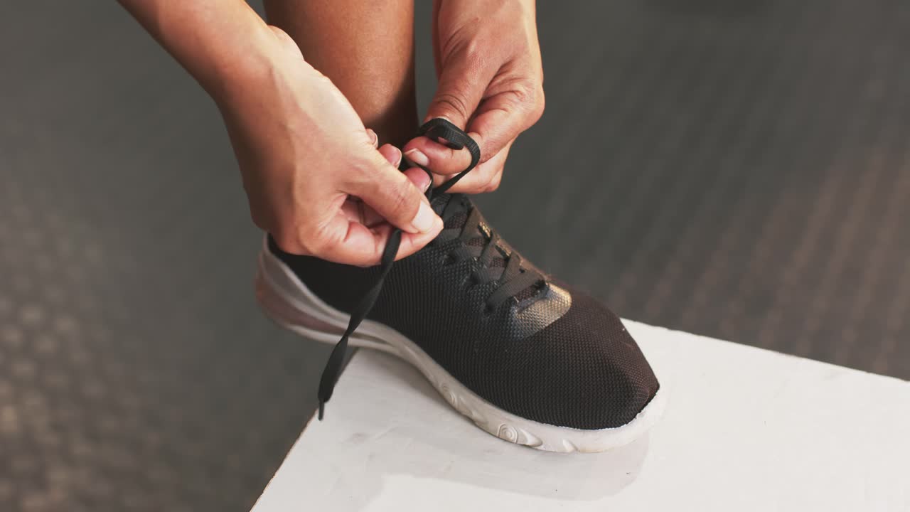 Con il piede appoggiato sulla panca, le mani allacciano i lacci neri delle scarpe da ginnastica per una calzata sicura