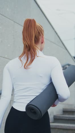 a dedicated fitness enthusiast, confidently carrying her yoga mat and water bottle, ready for a workout session in an urban setting with a stylish athletic outfit