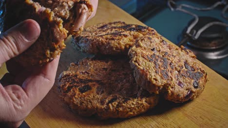 Hand-picking-up-and-breaking-a-crispy-fried-tuna-fritter-on-a-brown-board-with-three-other-fritters