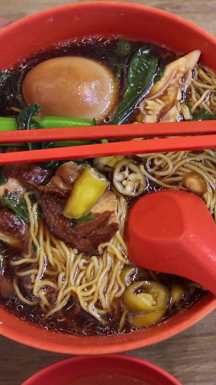 Una vista verticale dall'alto di una ciotola rossa piena di noodles, uovo e brodo.