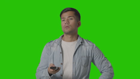 Studio-Shot-Of-Casually-Dressed-Young-Man-With-Remote-Control-Flicking-Through-TV-Channels-Against-Green-Screen-