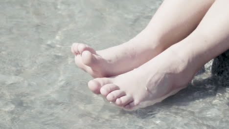 이탈리아 알프스의 계곡 한가운데 있는 바위에 앉아 다리와 발을 물에 담그고 있는 어린 소녀들