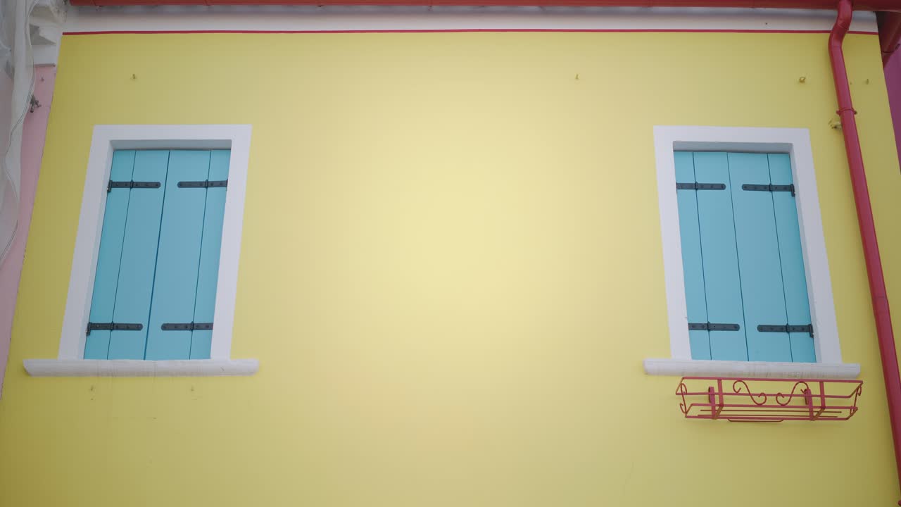 una casa de color amarillo vívido con persianas azules en burano, italia