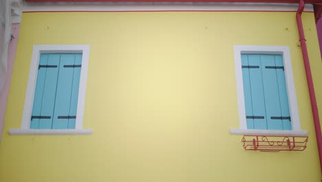 vividly painted yellow home with blue shutters in burano, italy