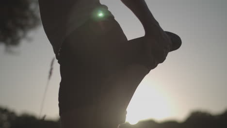 close up shot of a young man stretching before a run in the park whilst being silhouetted by the evening sun, in slow motion ungraded