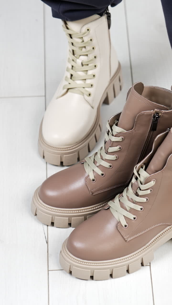 Model puts on the floor a similar beige pair of boots to those she's wearing. Female demonstrating stylish modern footwear. Top view. Vertical video