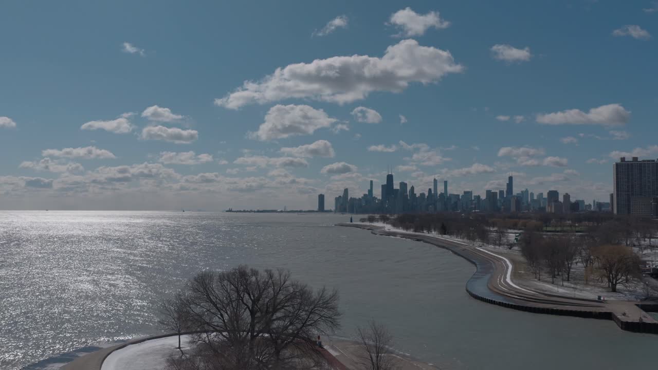 Uma bela tomada de drone em descida do horizonte de Chicago ao longo do Lago Michigan em um dia de inverno, enquanto a câmera desce para as árvores de Belmont Harbor em primeiro plano.