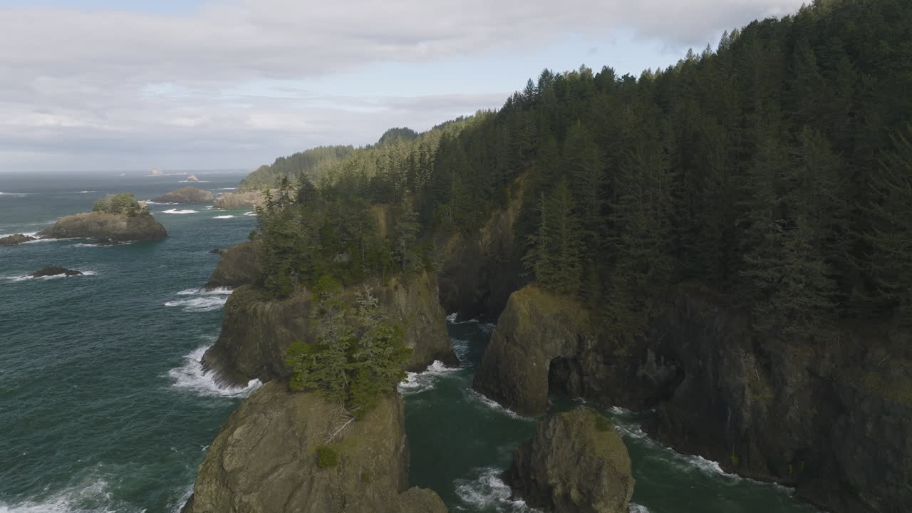 Panoramic aerial dolly overview of sea stacks with evergreen trees above towering natural bridges along Oregon Coast