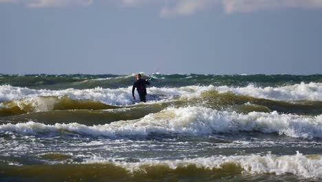 man on a kitesurfing board surfing on high waves of baltic sea, poland.