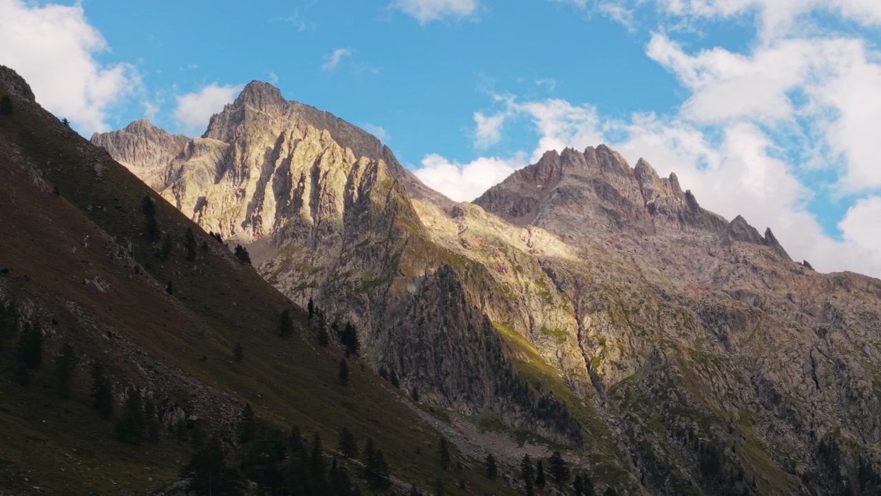 Sunlight illuminates rugged Dolomites peaks under blue sky with scattered clouds