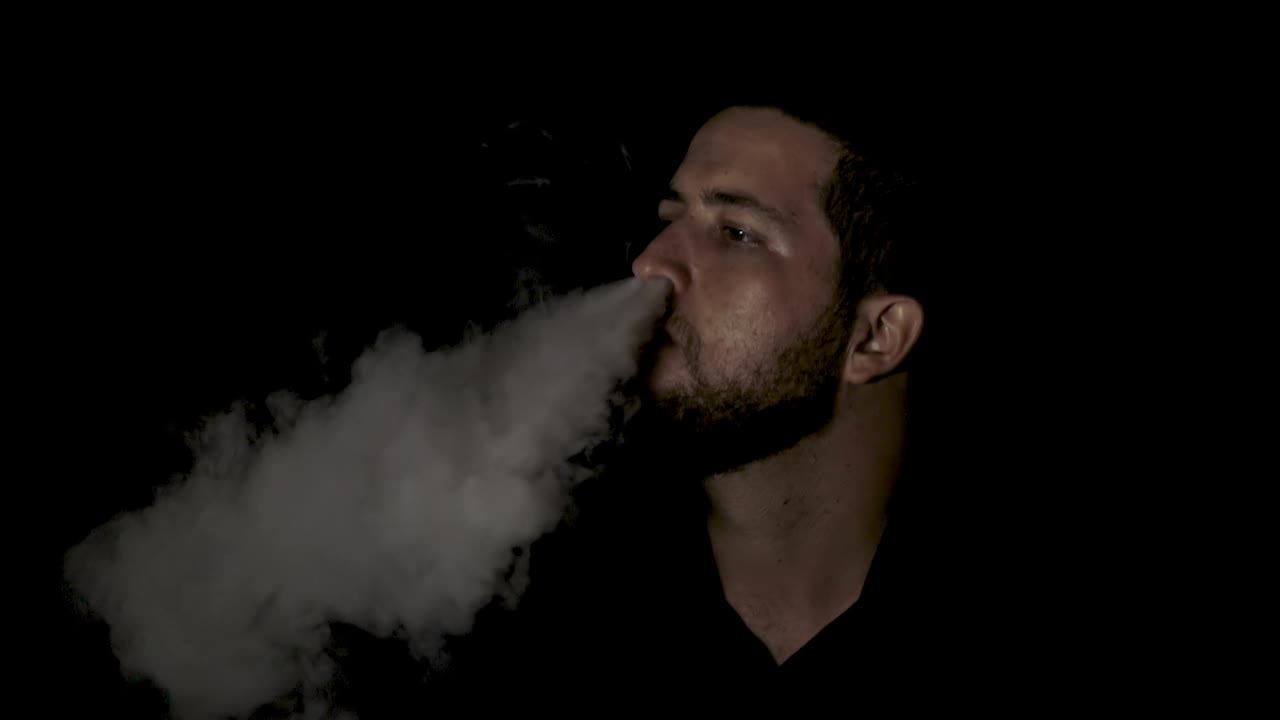 hombre fumando humo de su nariz sobre fondo negro, cámara lenta
