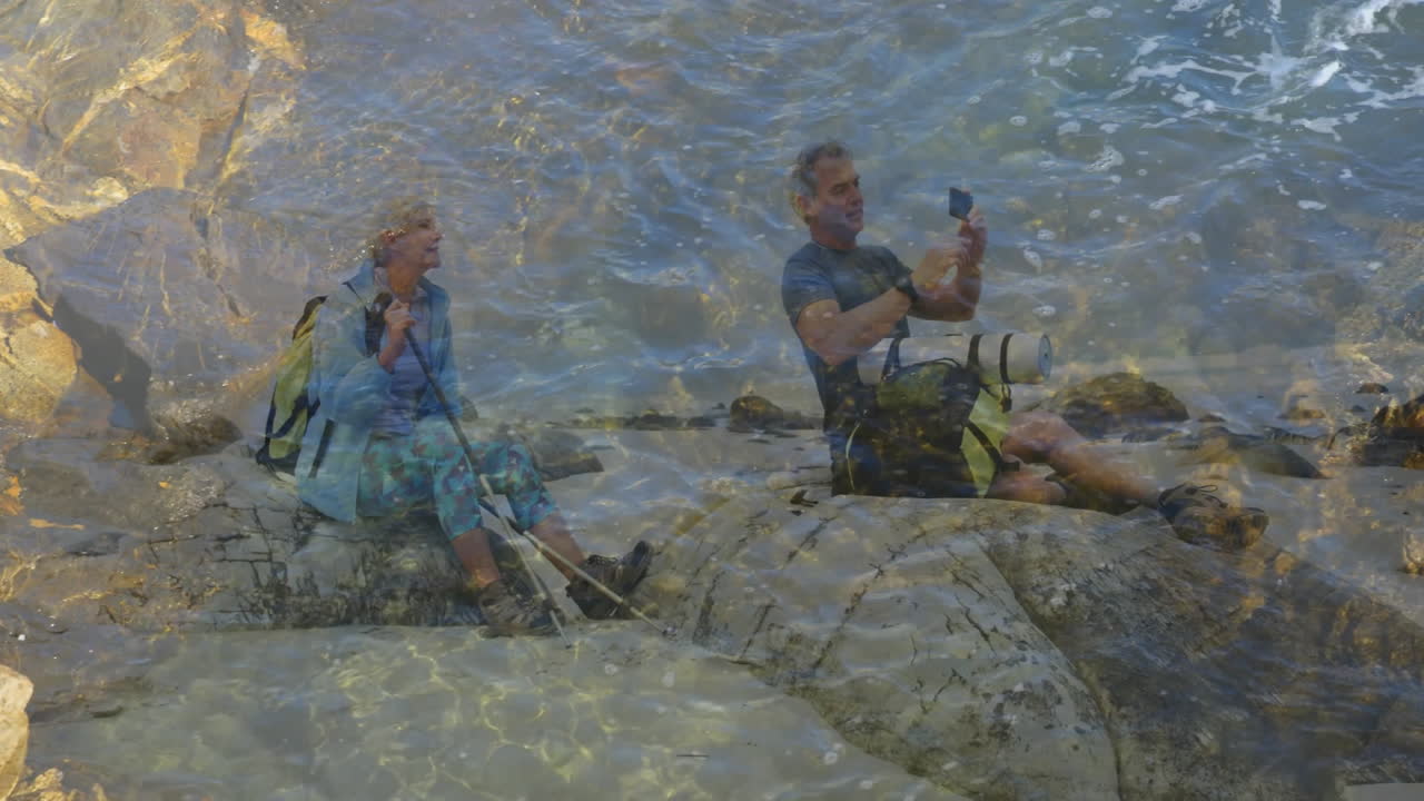 Hikers sitting on rocky shoreline tracking hiking stats with animated fitness graph and heart icon