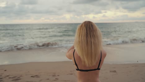 beautiful attractive woman in black bikini holds phone vertical taking video at beach with sunset