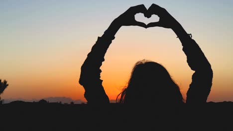 girl holding heart shape in the sunset / sunrise time.