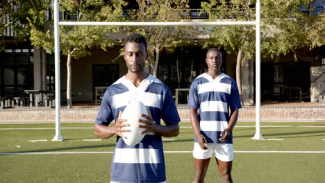 holding rugby ball, two african american men in sports uniforms standing on field, copy space