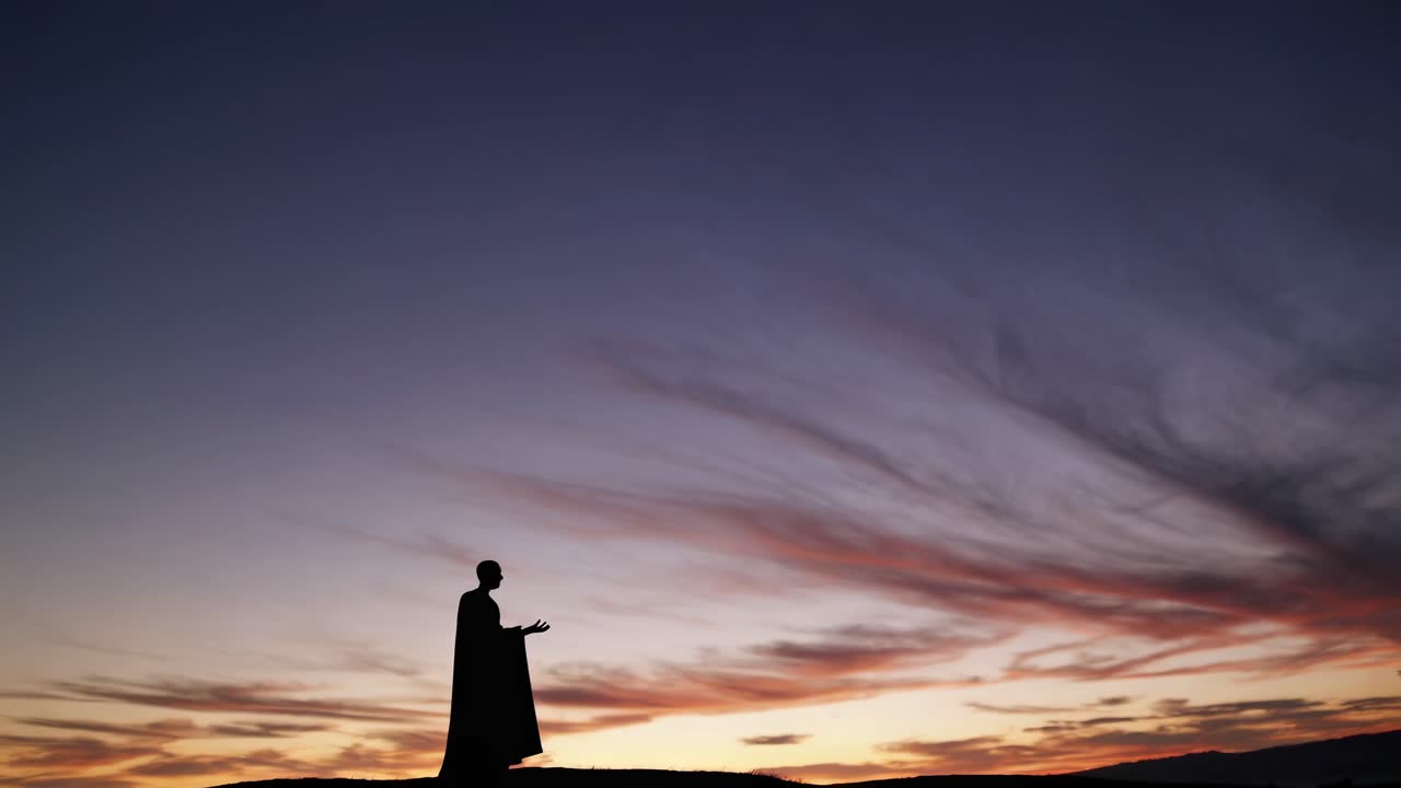 Silhouette of a person in a cape at sunset, shot from a low angle