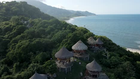 Drone-aerial-shot-over-the-small-huts-of-the-Tayrona-rainforest-overlooking-the-ocean-in-Colombia